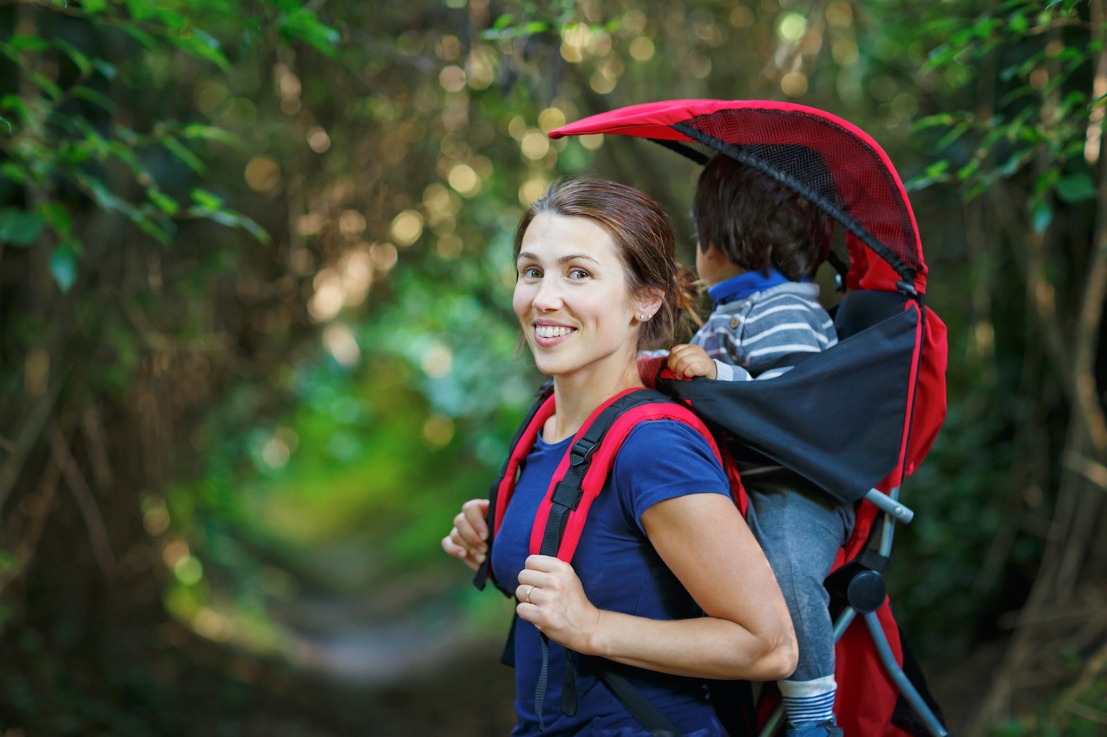 Mother with toddler child in backpack carrier is hiking in forest